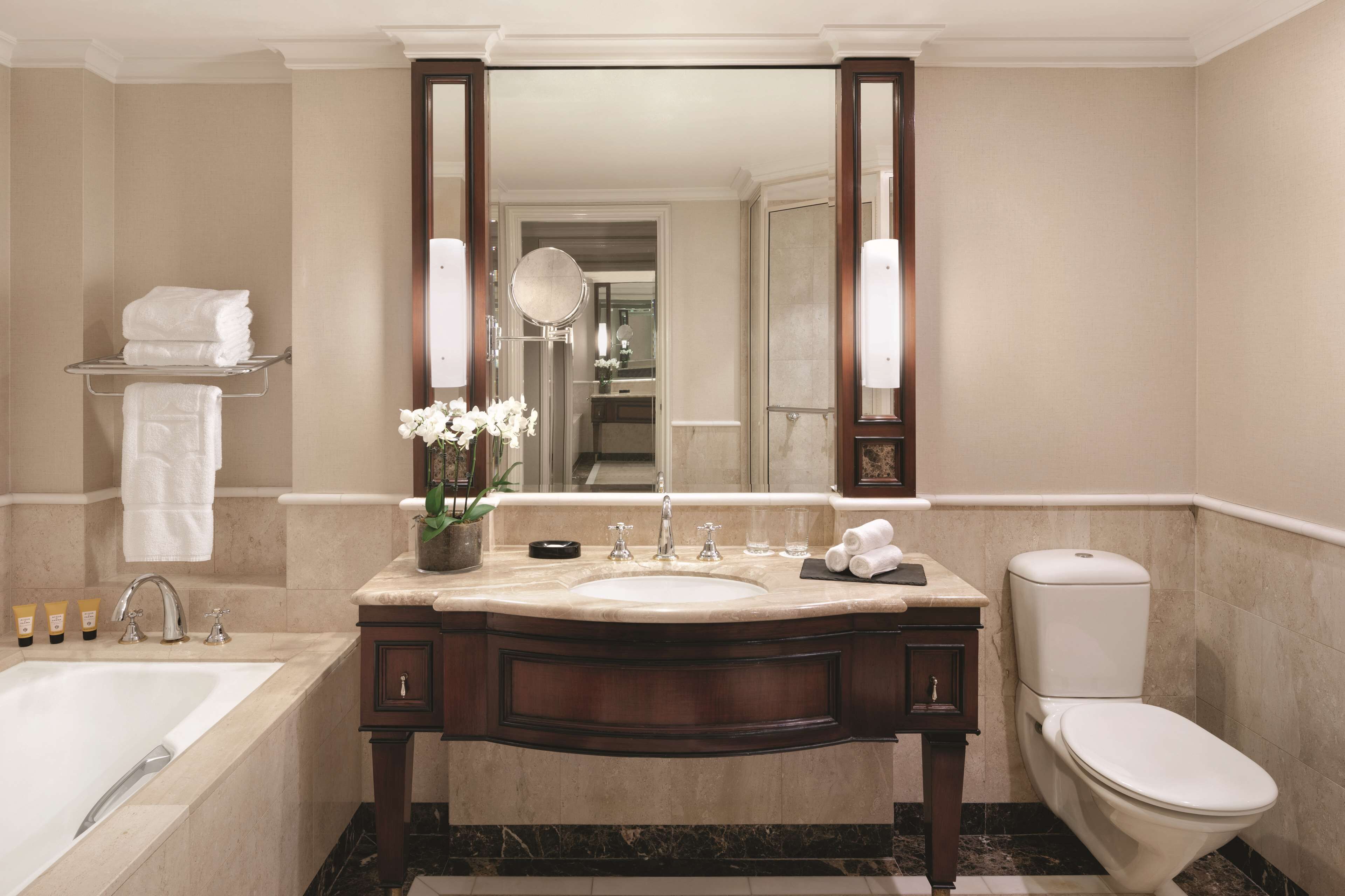 A modern bathroom with a large mirror, a bathtub, a toilet, and a vanity with a sink.
