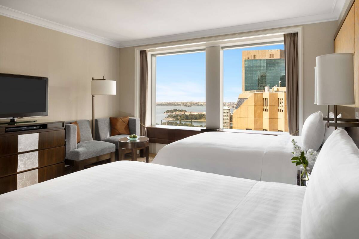 A hotel room with two beds, a TV, a desk, and a view of a cityscape.