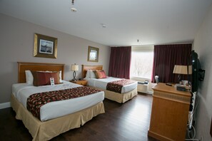 Een hotelkamer met twee bedden, een houten bureau, een telefoon en een raam met gordijnen.