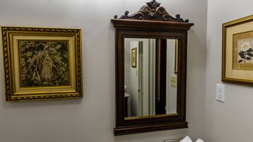 Un baño con inodoro, lavabo y espejo de tocador. Hay luces empotradas sobre el espejo y cuadros en las paredes.