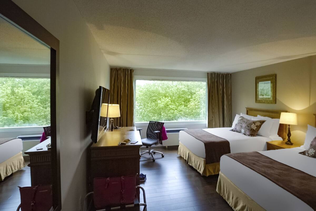Una habitación de hotel con dos camas, un escritorio con silla, televisión y ventana con cortinas.