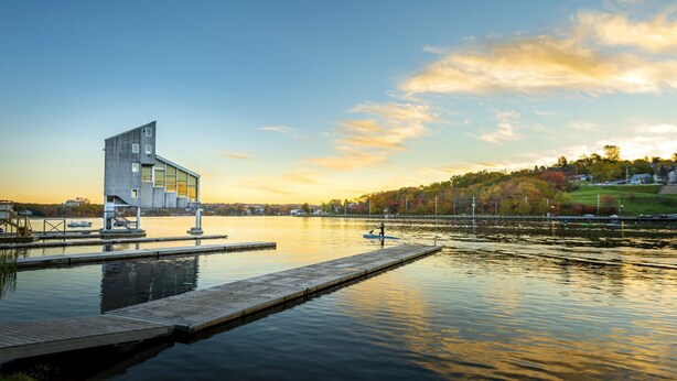 Un edificio moderno con un diseño angular único, ubicado junto a un lago tranquilo con un muelle que se adentra en el agua.