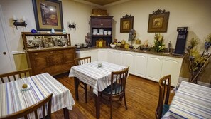 Een eetgedeelte met houten tafels en stoelen, een keuken met kasten en apparatuur, en een wand met ingelijste foto's en wandlampen.