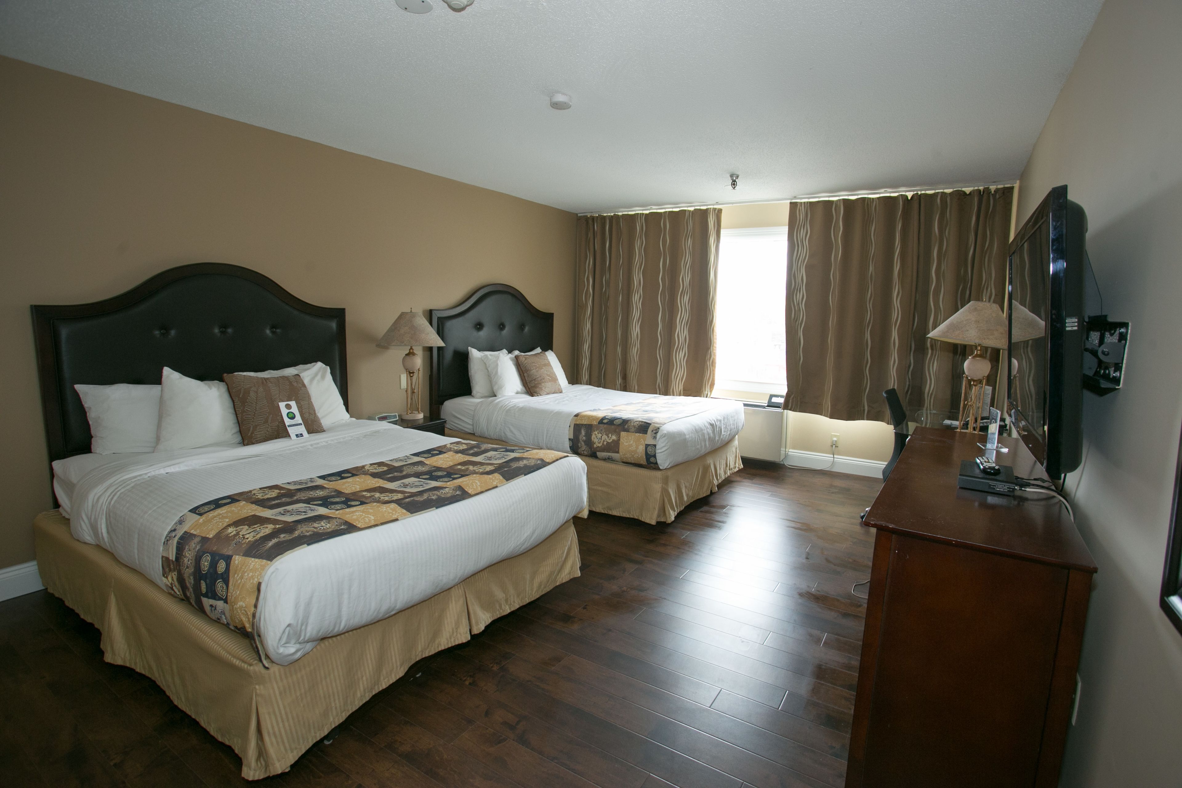 Habitación de hotel con dos camas, suelo de madera, cómoda y ventana con cortinas.