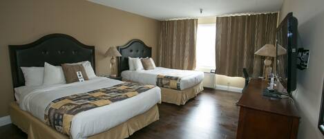 Habitación de hotel con dos camas, suelo de madera, cómoda y ventana con cortinas.
