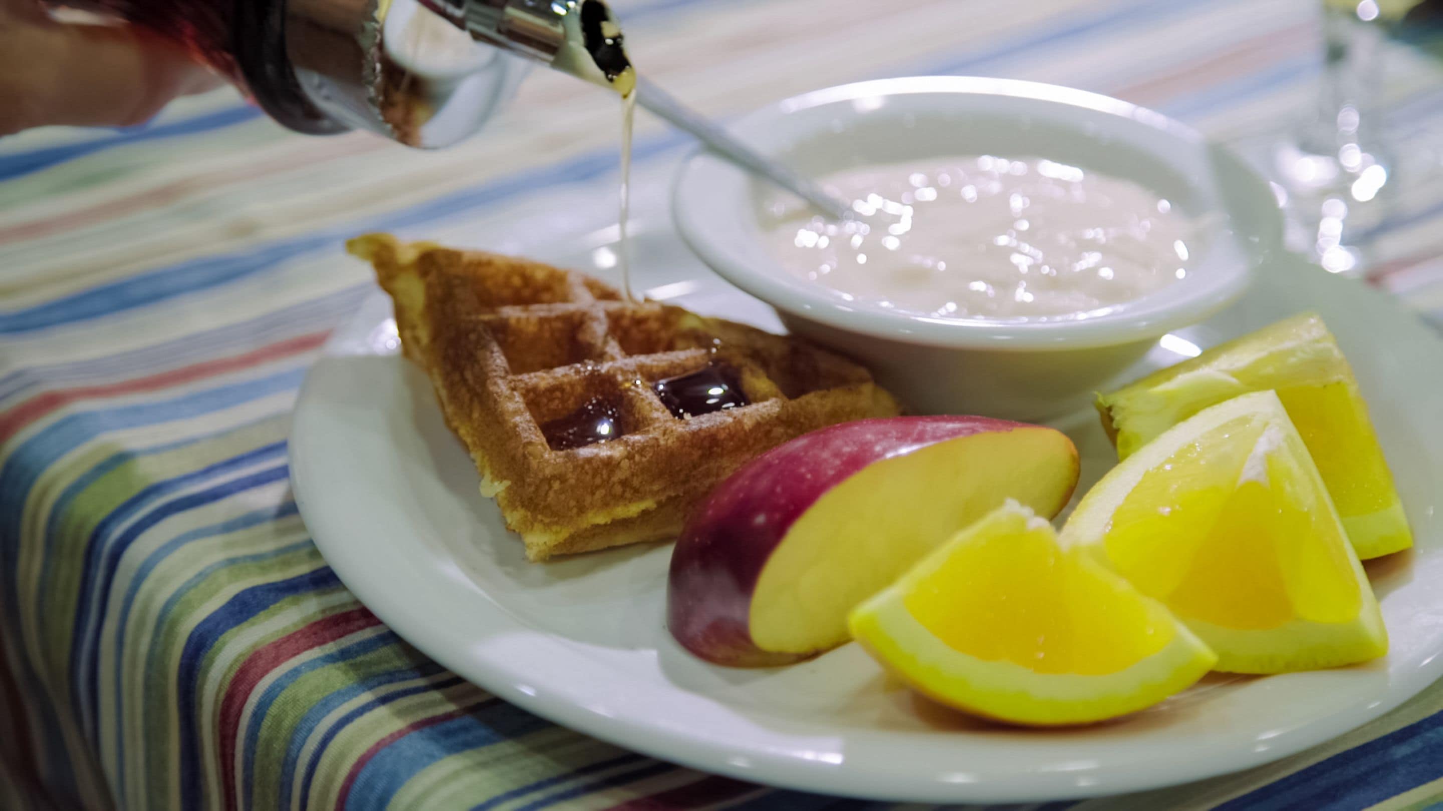 A plate with waffles, a bowl of yogurt, and sliced fruits.
