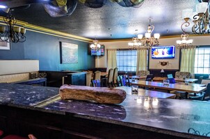 Un restaurante con zona de bar, varias mesas y sillas. Hay televisores montados en las paredes y un candelabro colgando del techo.