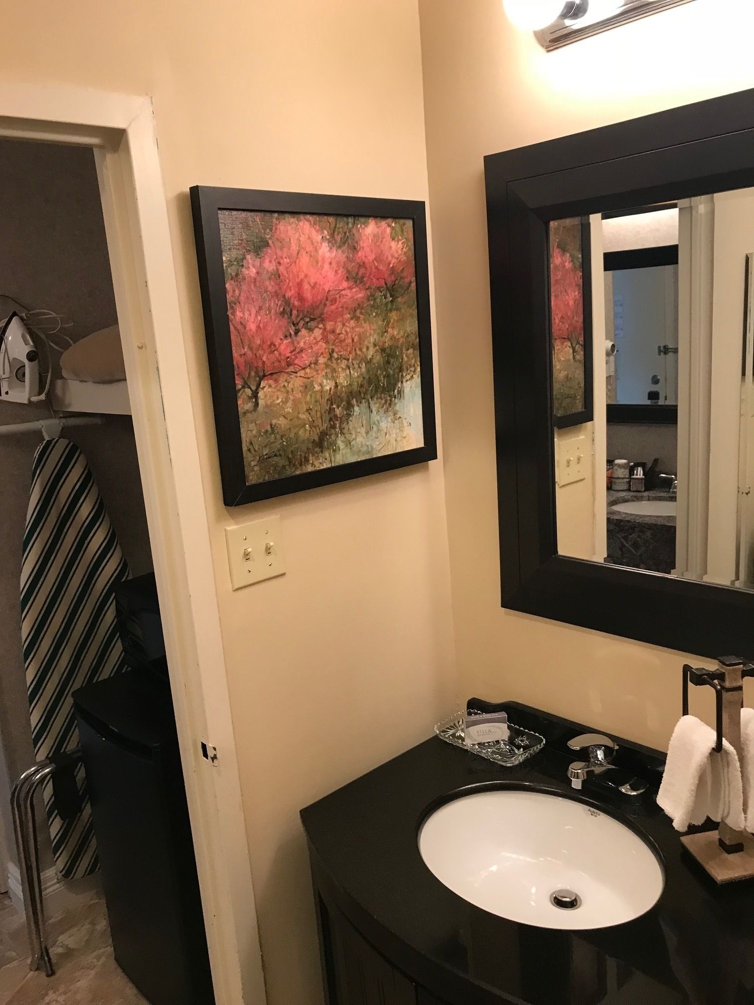 A bathroom with a black sink, a mirror, and a framed painting of pink flowers on the wall.
