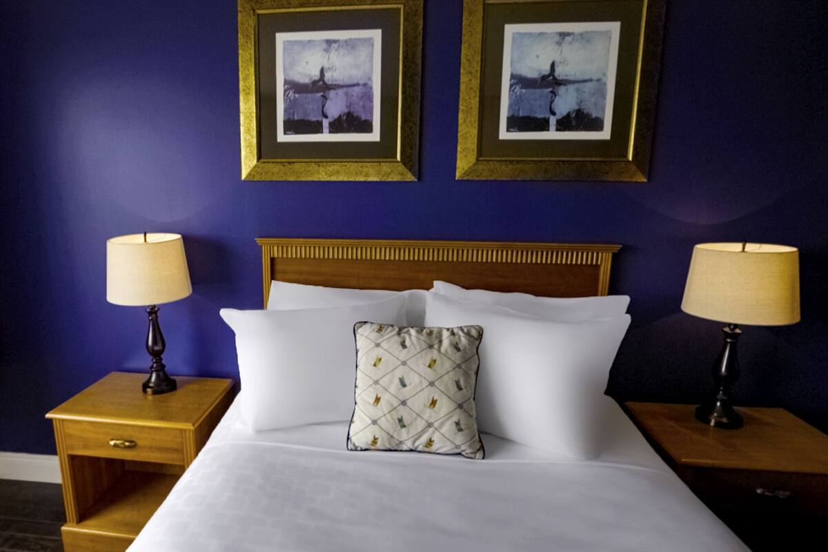 Habitación de hotel con una cama grande, dos mesitas de noche, dos lámparas y dos cuadros en la pared.
