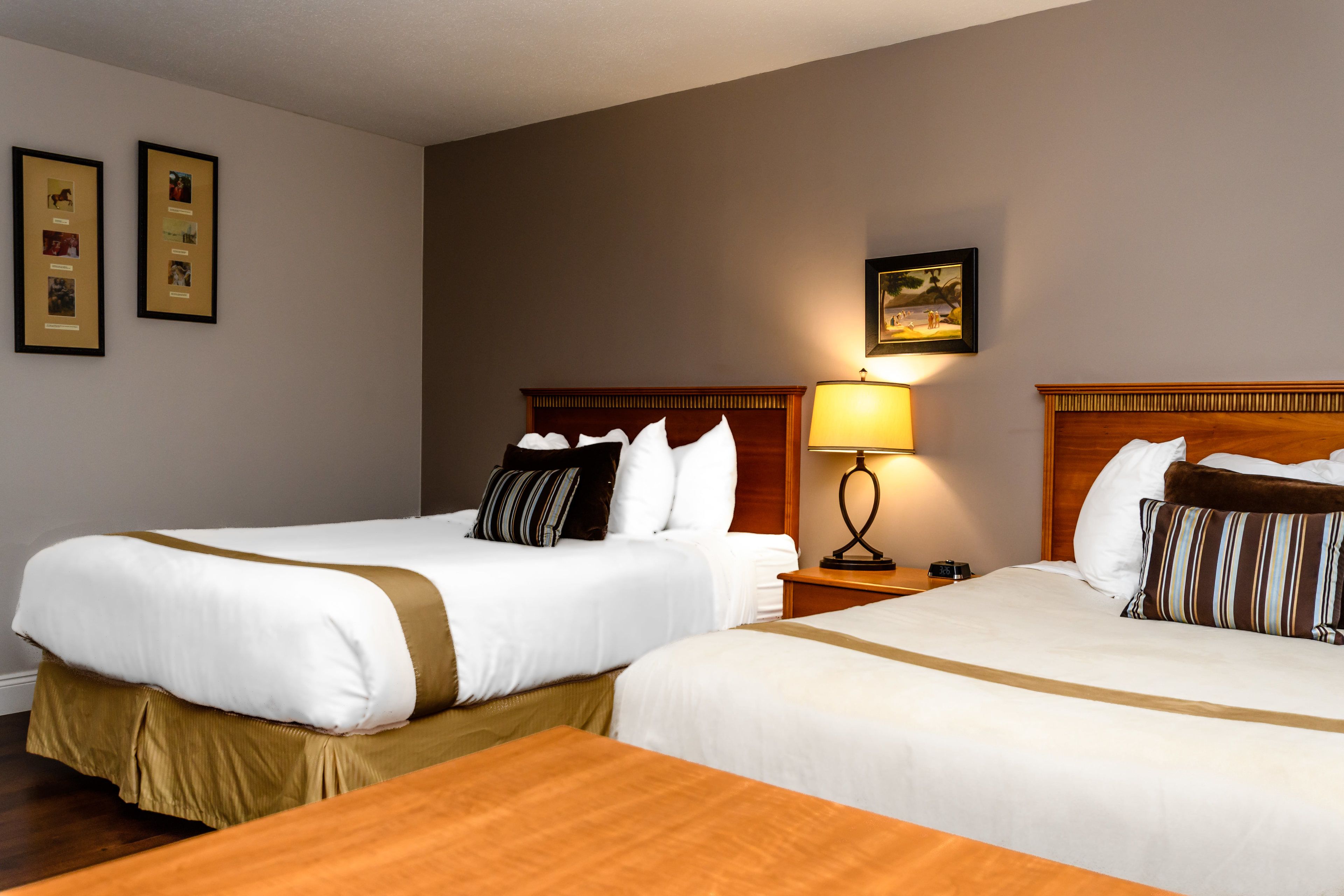 A hotel room with two beds, a nightstand with a lamp, and framed pictures on the wall.