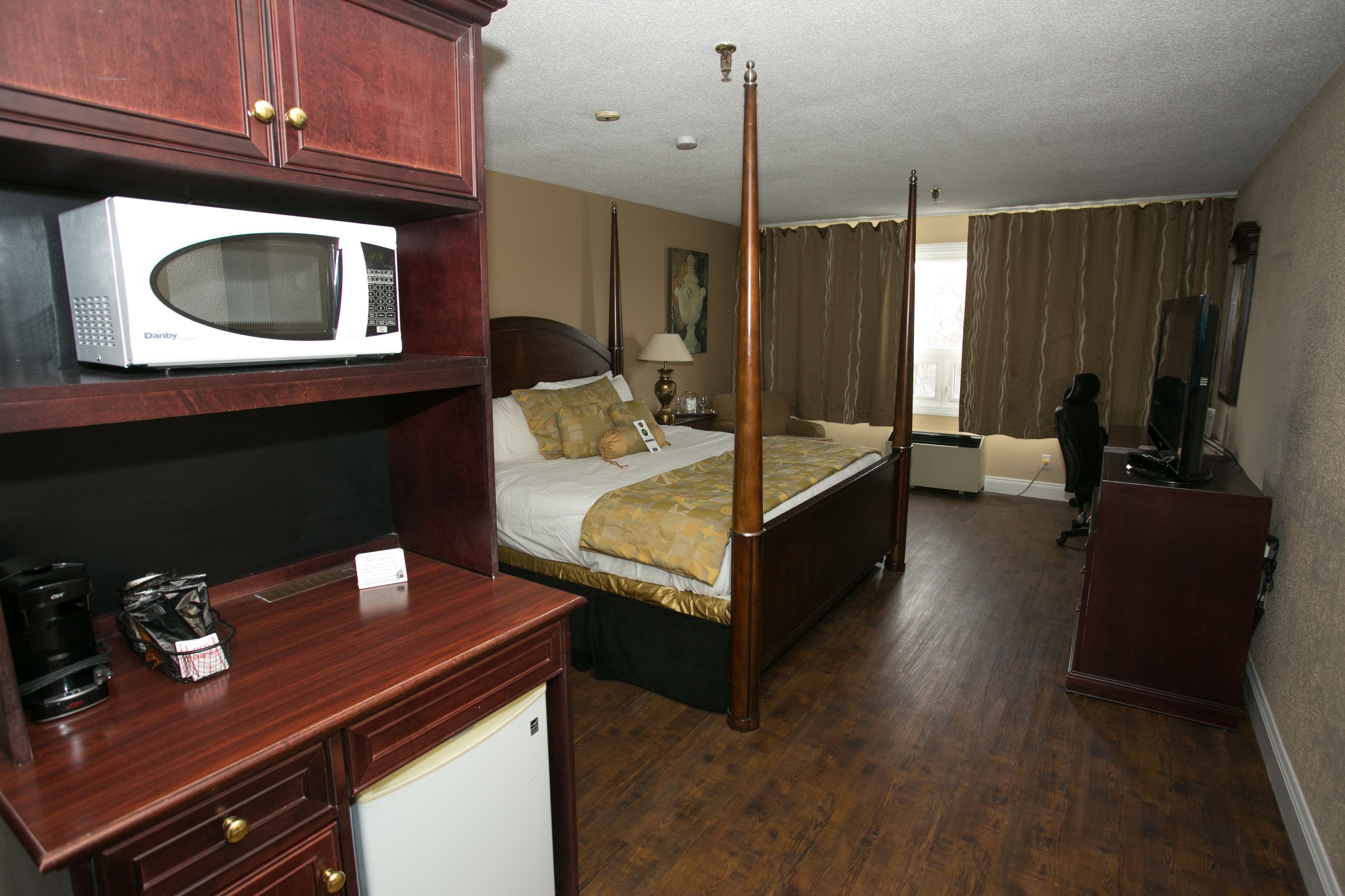Habitación de hotel con cama con dosel, microondas en un estante, escritorio con cafetera y televisión.