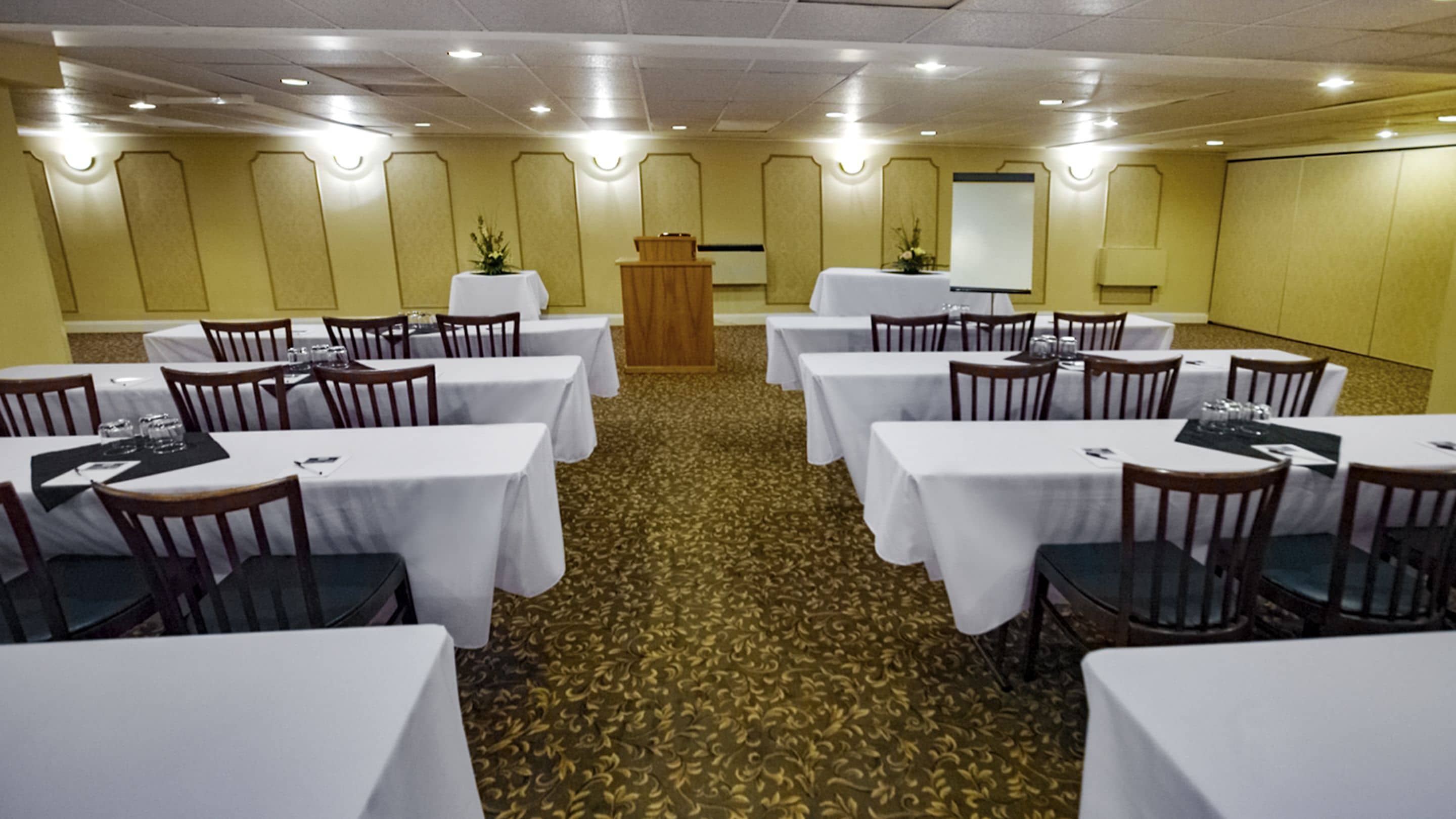 Un salón de conferencias con varias mesas y sillas, un atril y suelo alfombrado.