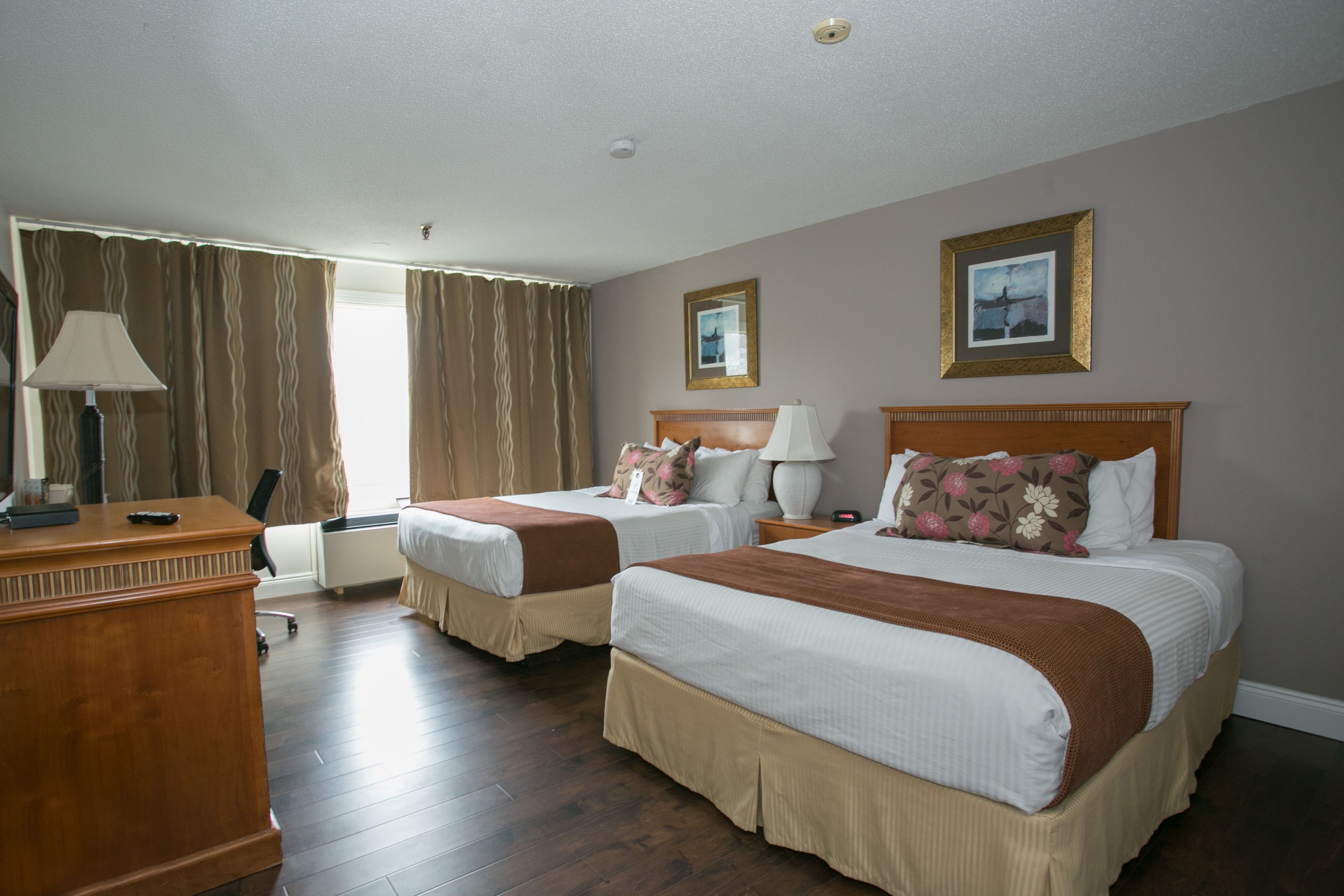 A hotel room with two beds, a desk, a lamp, and a window with curtains.