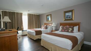 A hotel room with two beds, a desk, a lamp, and a window with curtains.