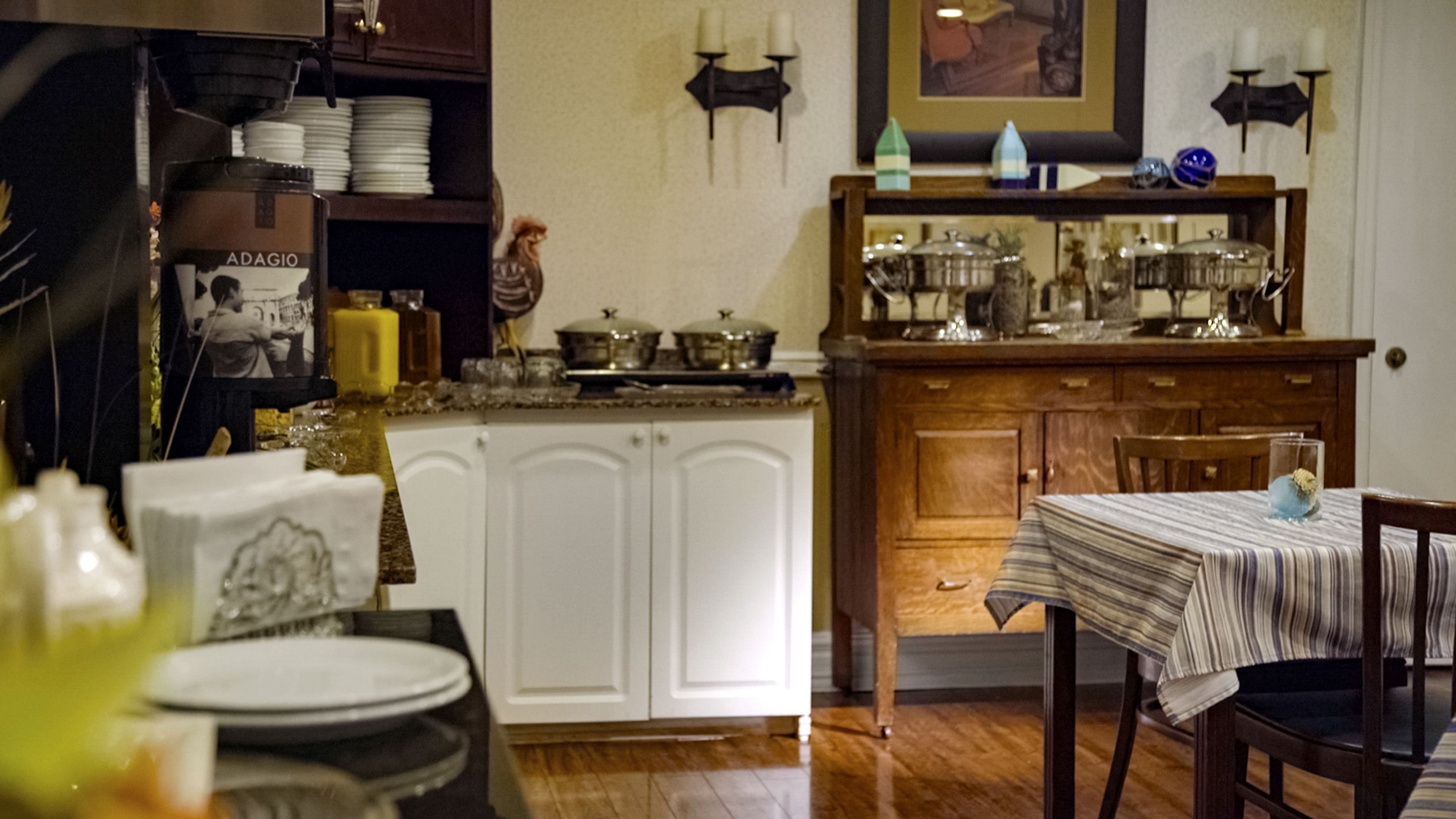Una cocina con armarios blancos, una mesa de comedor con mantel a rayas y varios utensilios de cocina sobre la encimera.
