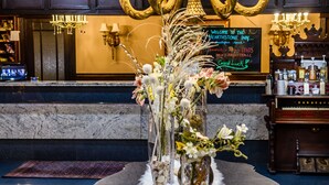 Un vestíbulo con una imponente lámpara de araña, un mostrador de recepción y un jarrón decorativo con flores.