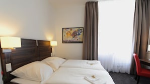 Habitación de hotel con cama, dos lámparas de noche, un cuadro en la pared y una silla roja.