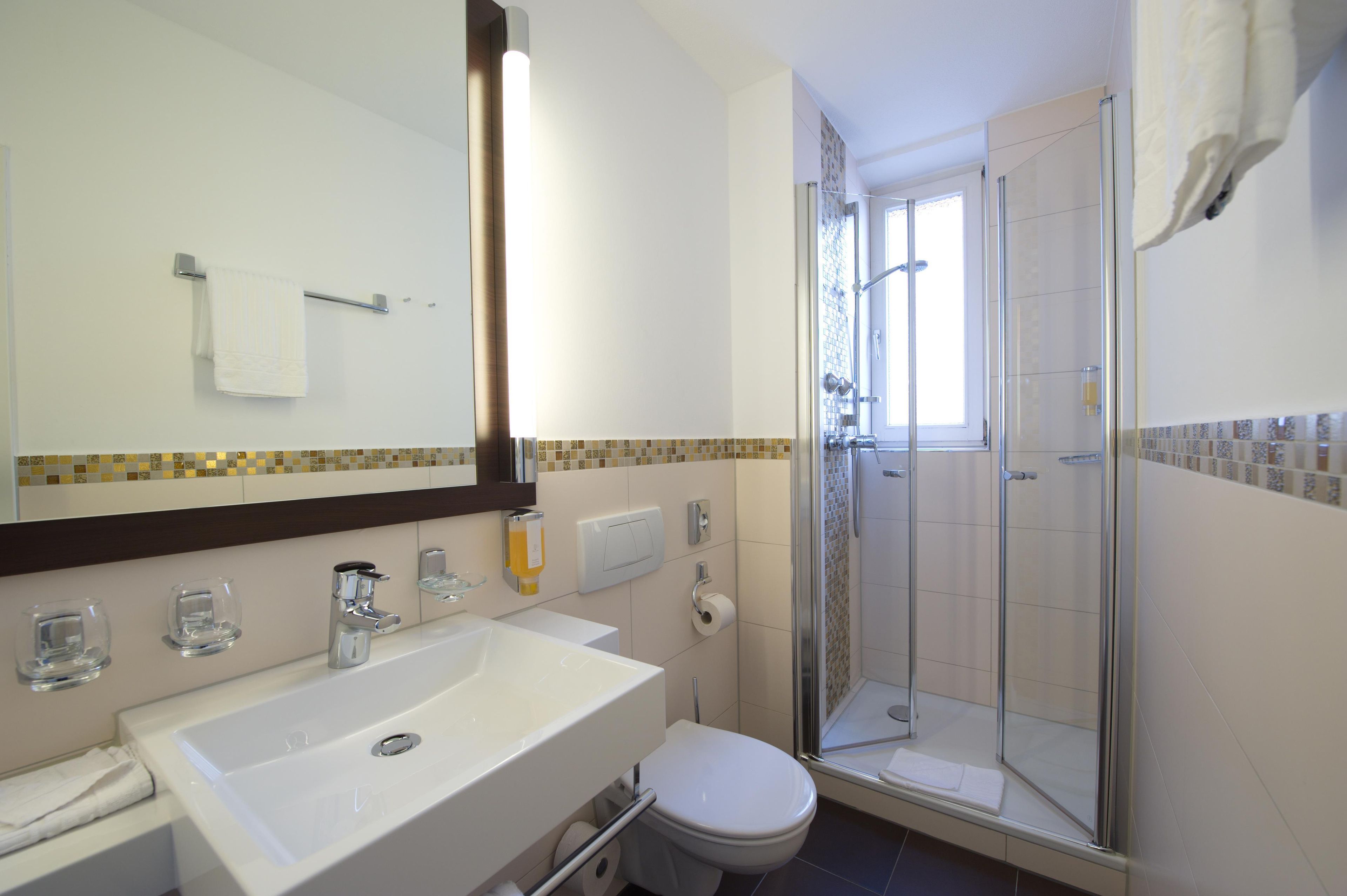 Ein Badezimmer mit einem weißen Waschbecken, einer Toilette, einer Duschkabine aus Glas und einem Spiegel mit einem Handtuch an der Wand.