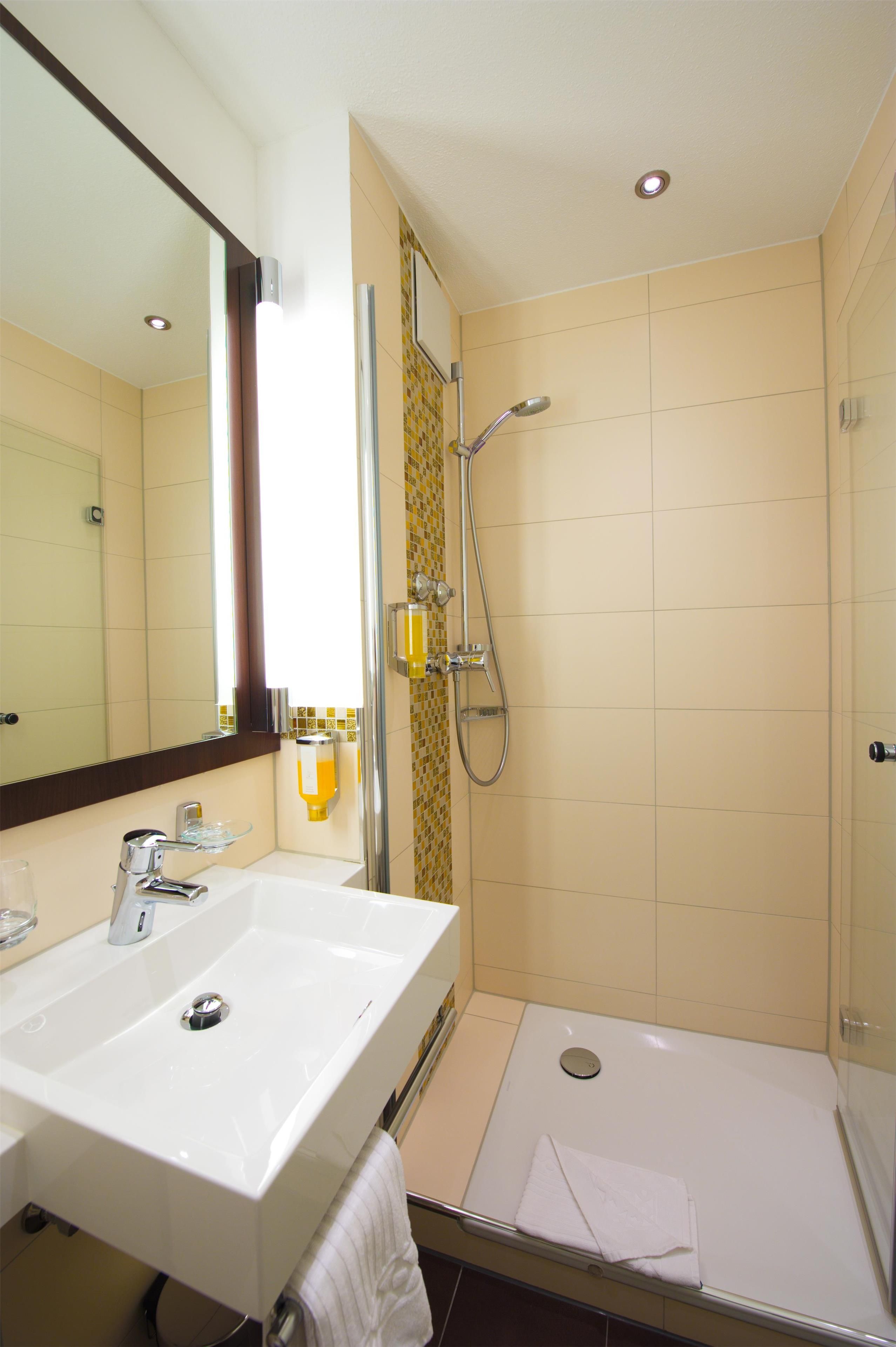 A bathroom with a sink, mirror, shower, and toilet.