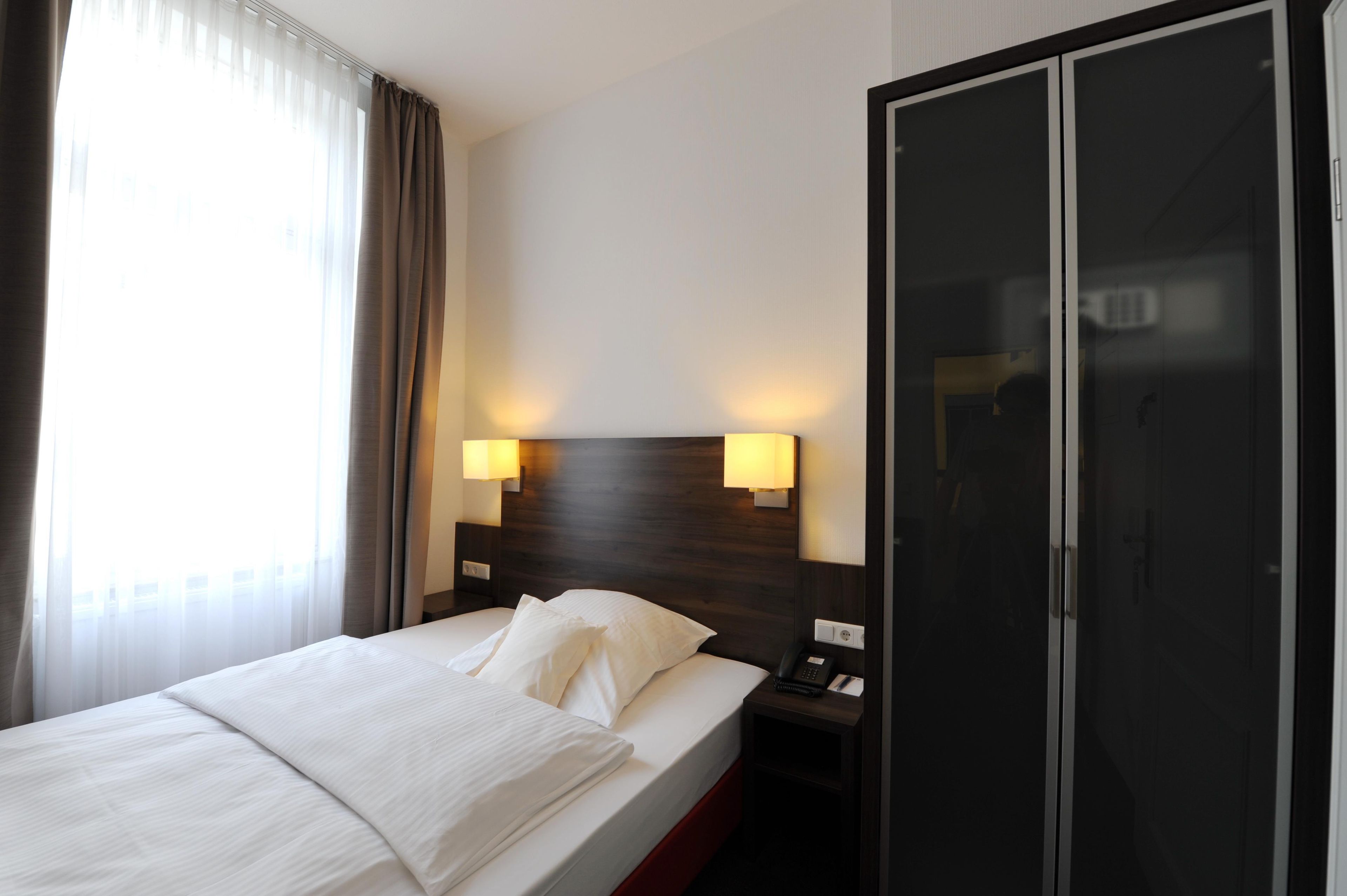 A hotel room with a bed, bedside lamps, a wardrobe, and a window with curtains.
