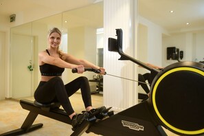 A woman using a rowing machine in a gym with a mirror and exercise equipment in the background. - Best Western Hotel Kaiserhof (Bonn)