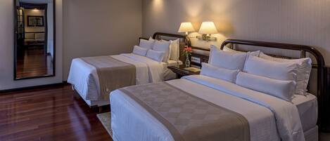 A hotel room with two beds, a nightstand with lamps, a mirror, and a wooden floor.