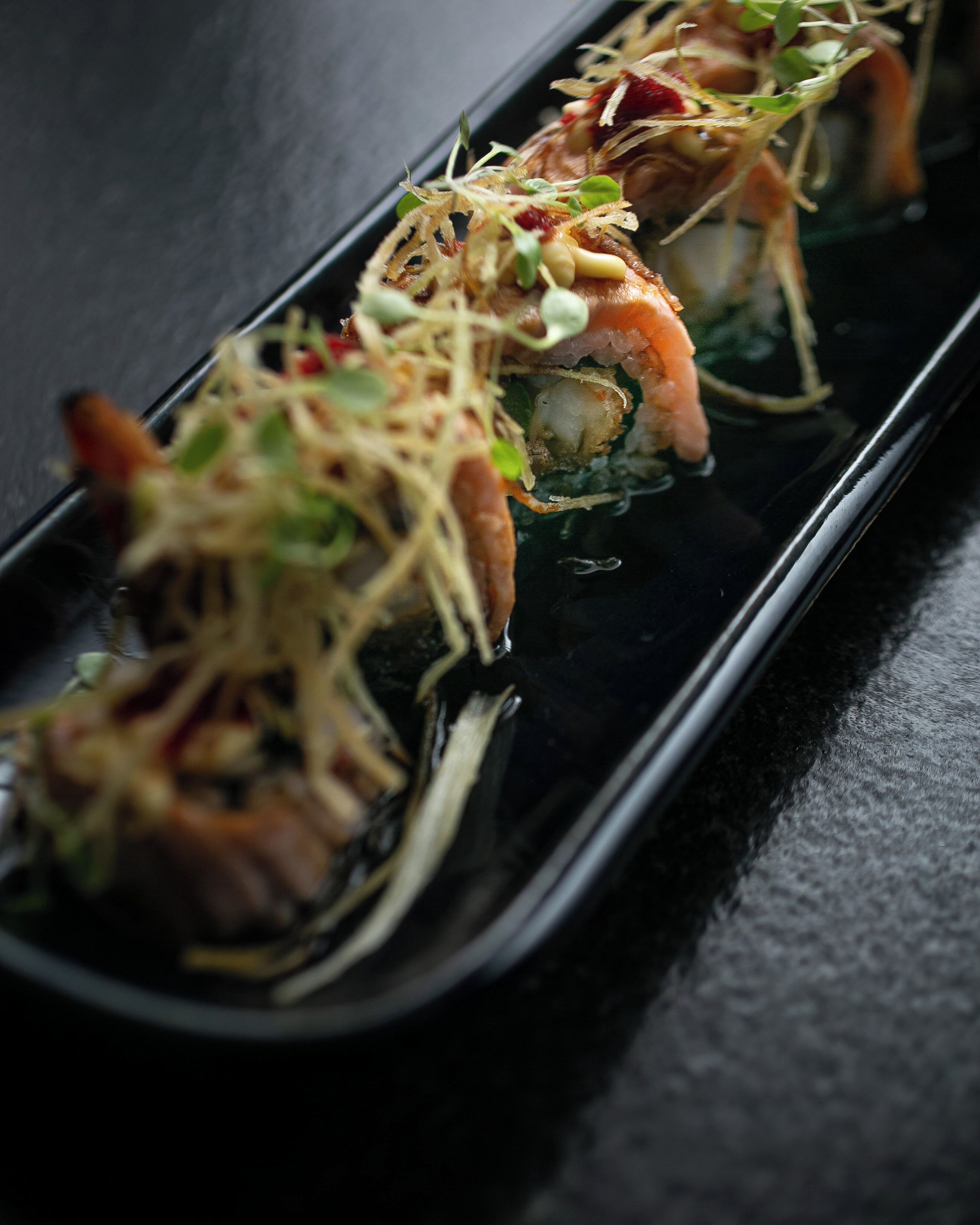 Een sushi gerecht met garnalen en groenten op een zwart bord.