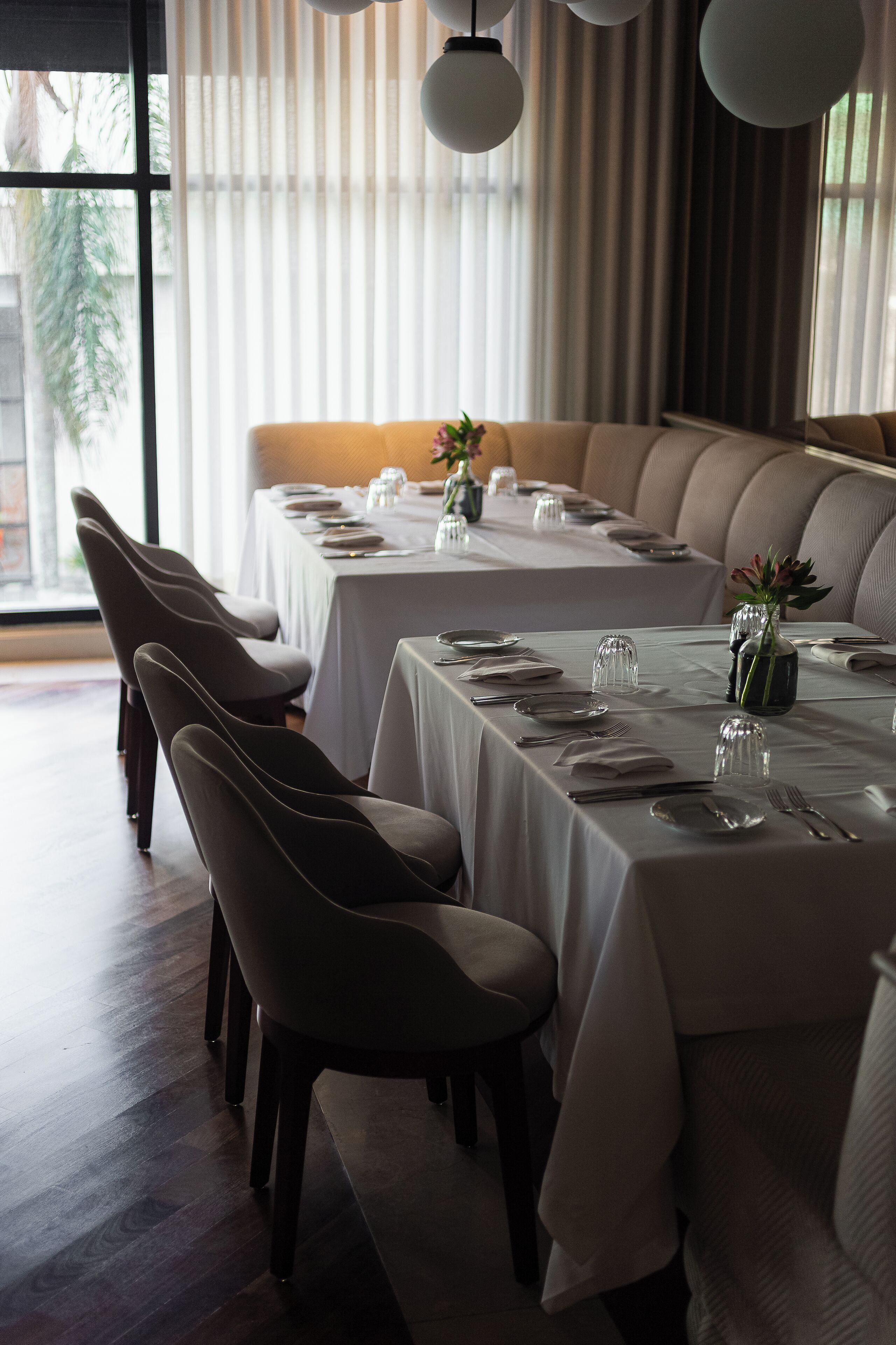 Un restaurante con mesas largas dispuestas para comer, sillas y un jarrón con flores sobre la mesa.