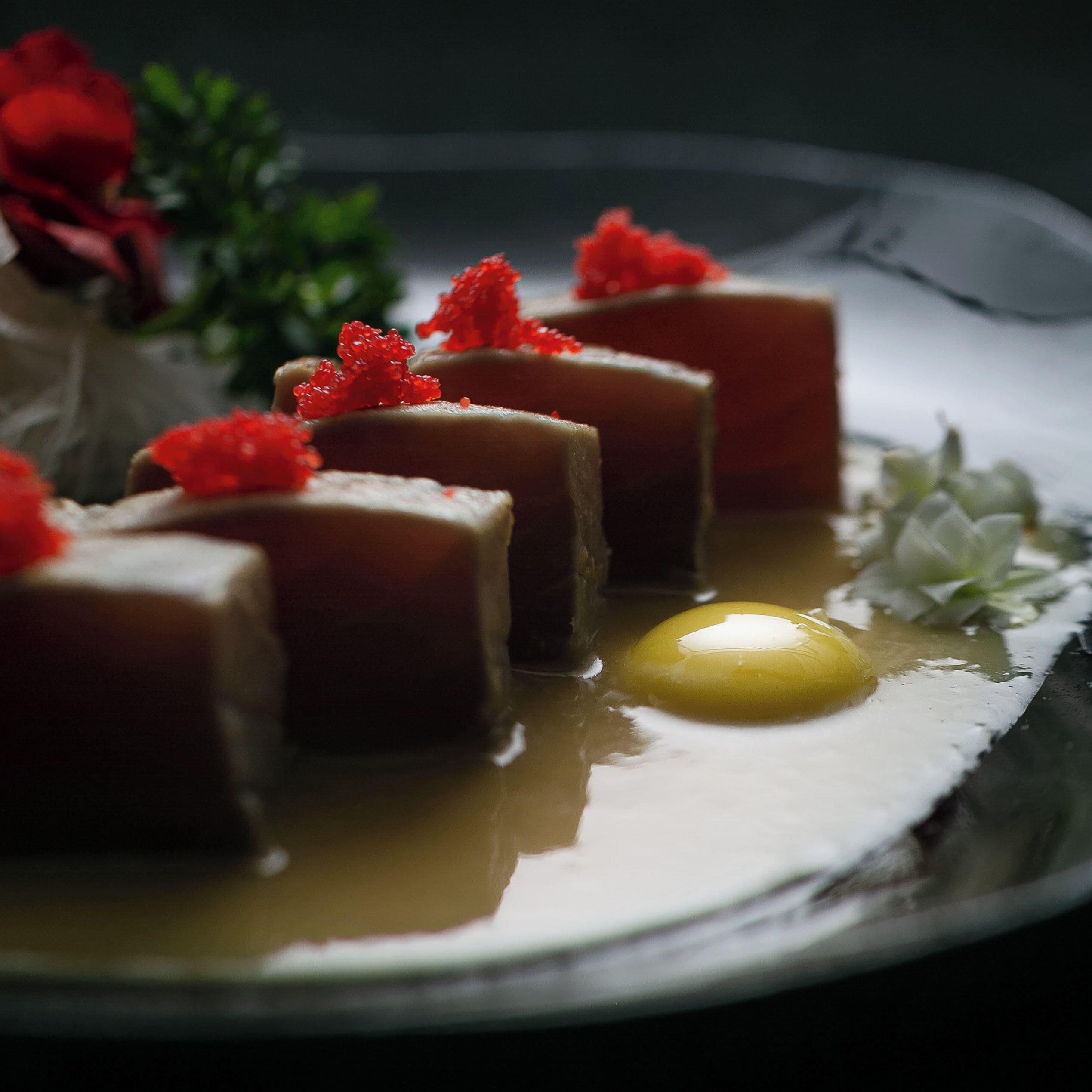 A dessert plate with several square-shaped items topped with red caviar, a single egg yolk, and some green garnish.