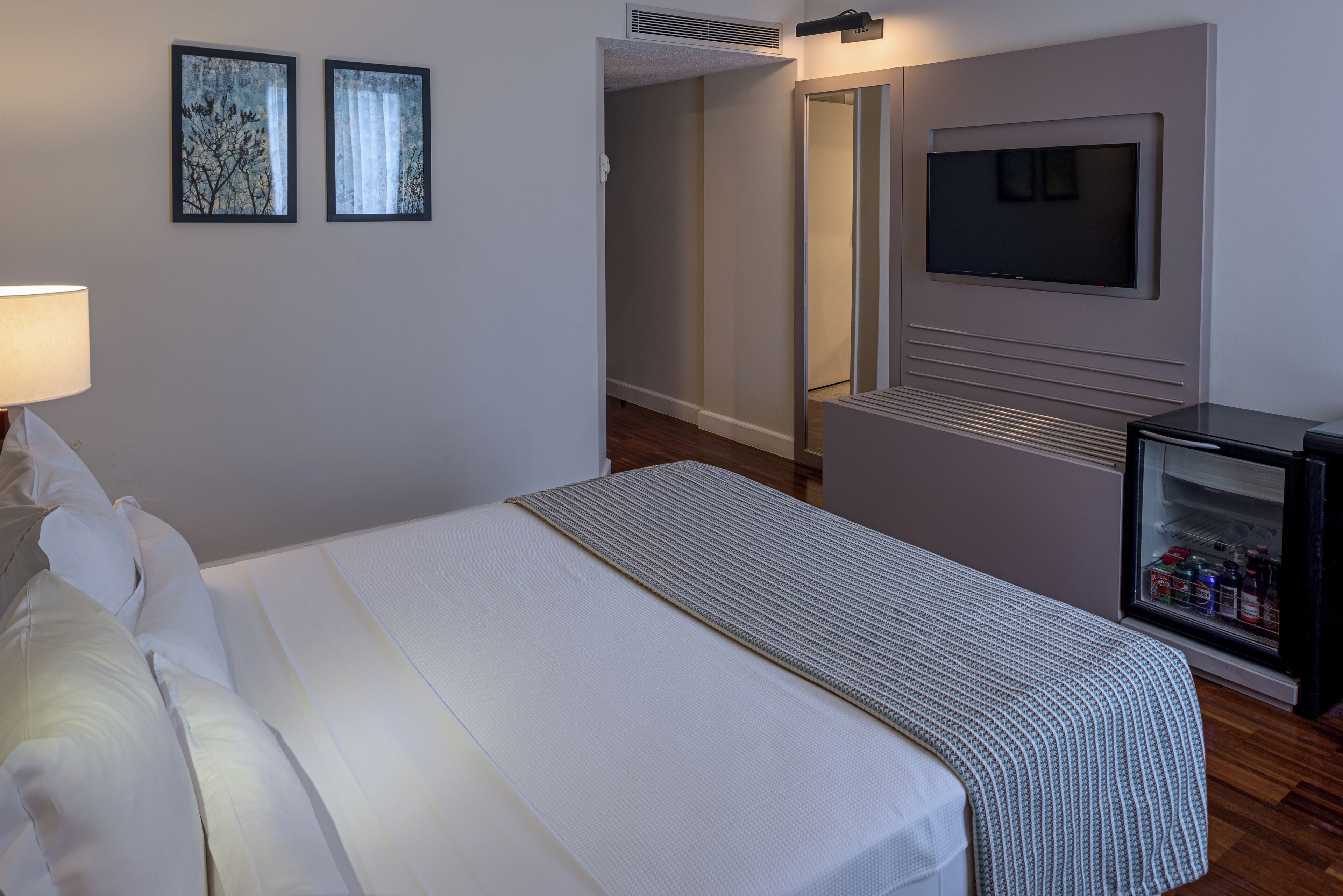 Habitación de hotel con una cama, televisor montado en la pared y un minibar.