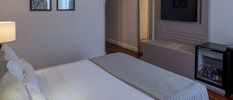 Habitación de hotel con una cama, televisor montado en la pared y un minibar.