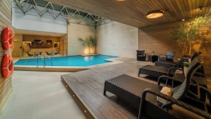 An indoor swimming pool with lounge chairs and a reception area.
