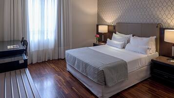 Une chambre d’hôtel avec un lit, des tables de chevet, un bureau et une fenêtre avec des rideaux.