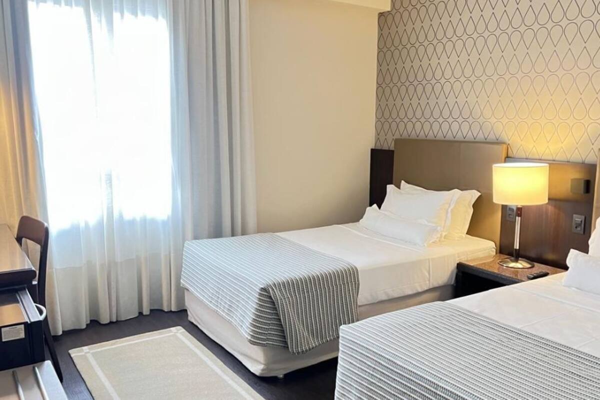 Habitación de hotel con dos camas, un escritorio, una lámpara y un papel tapiz estampado.