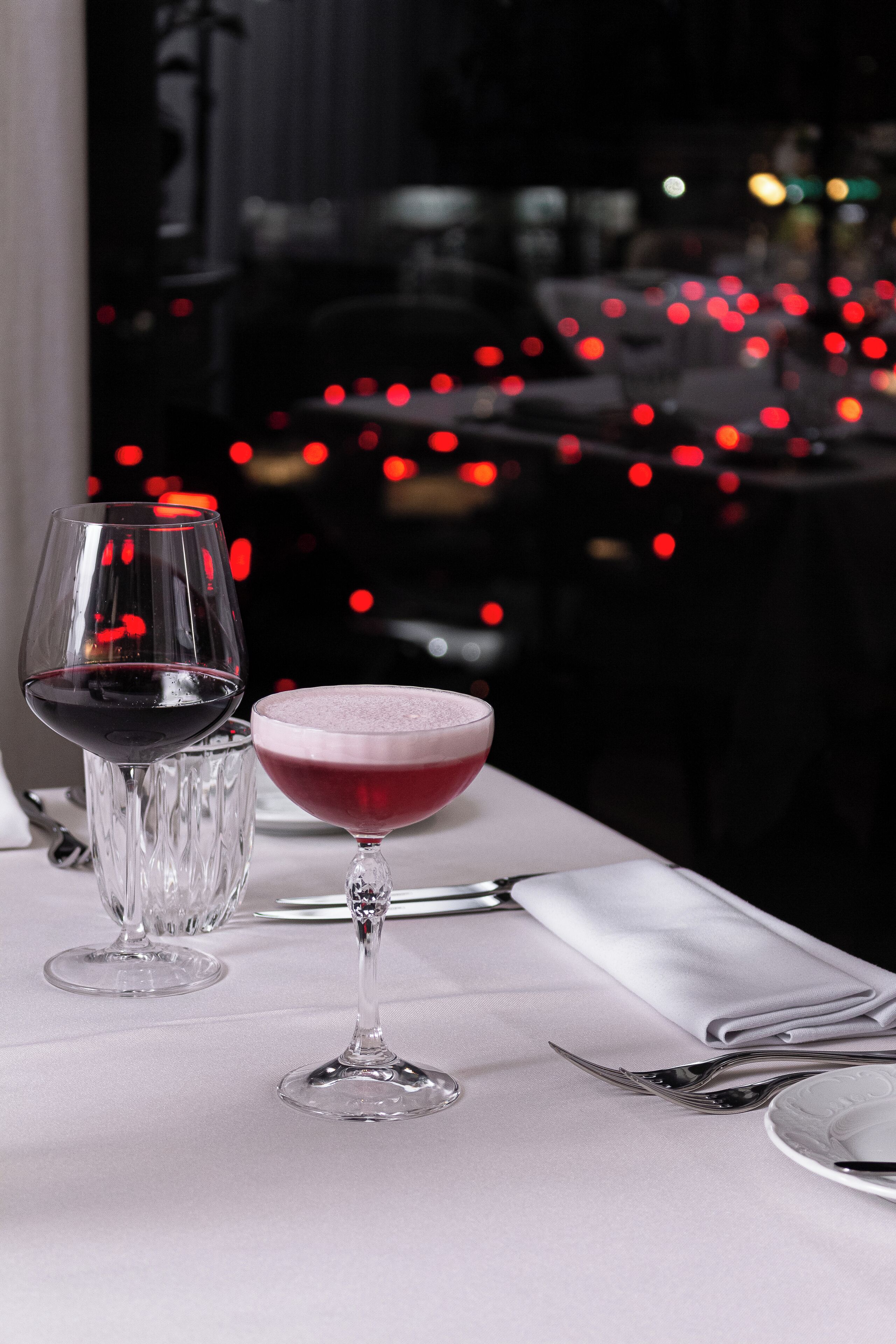 A table set with a wine glass and a cocktail glass, with a blurred background of lights.