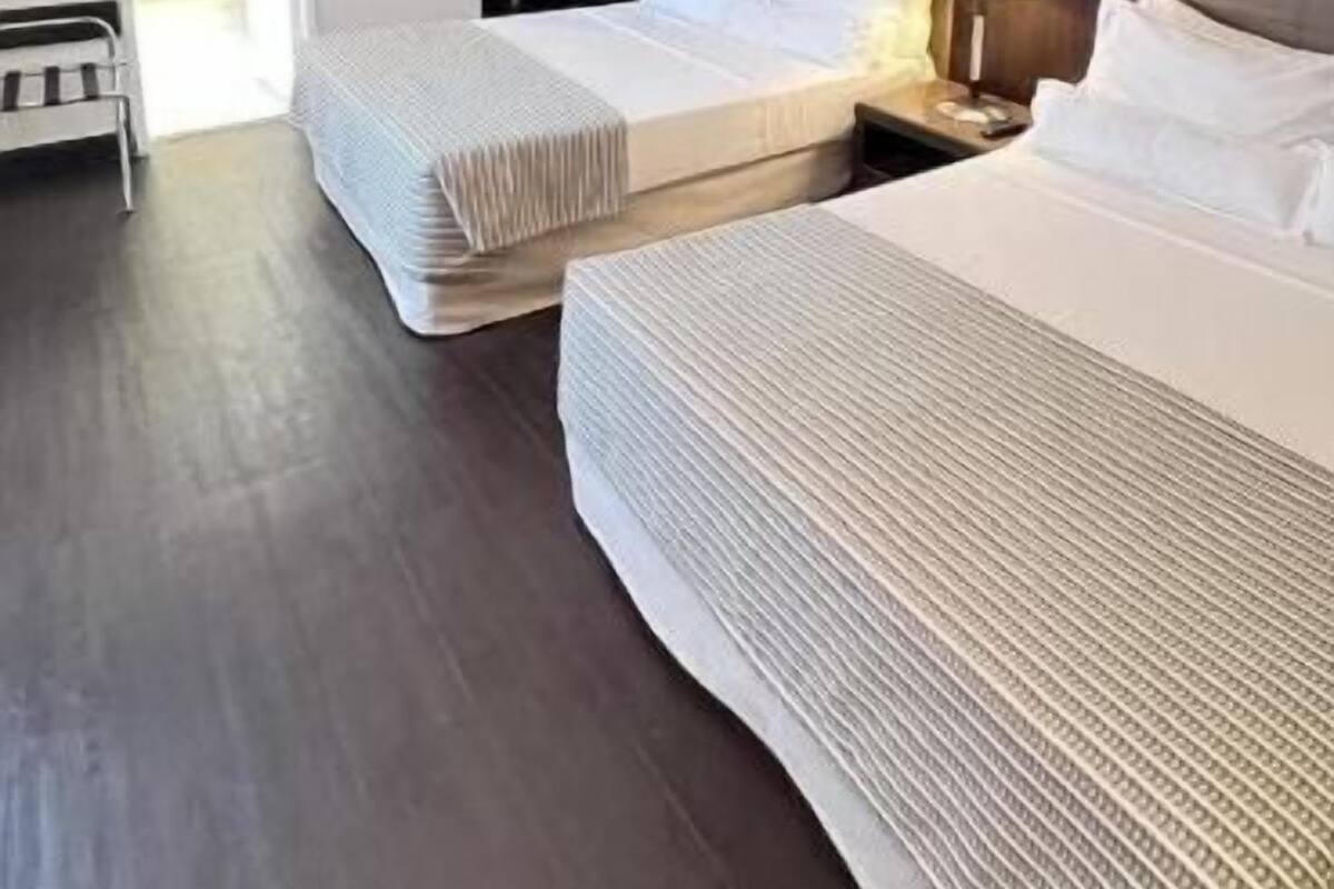 Habitación de hotel con dos camas, una mesita de noche con lámpara, cabecero y pared con estampado.