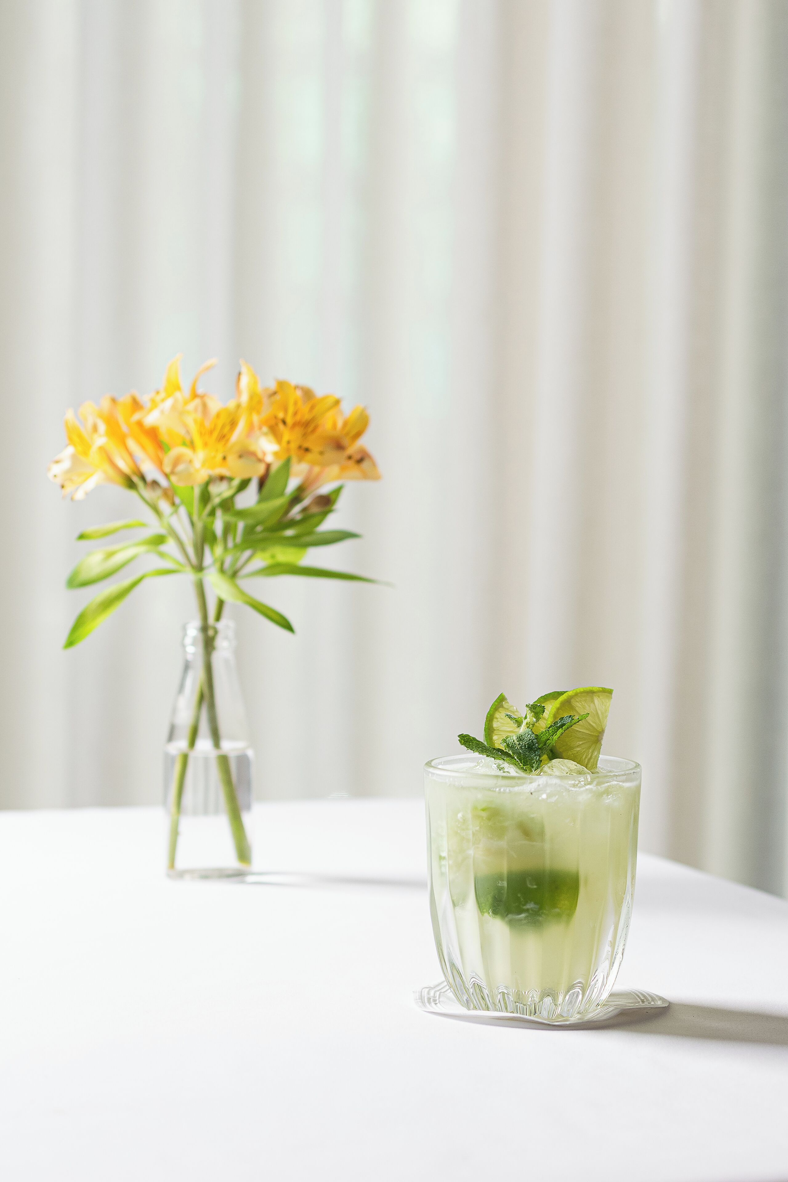 A clear glass with a lime slice and mint garnish on a white table.