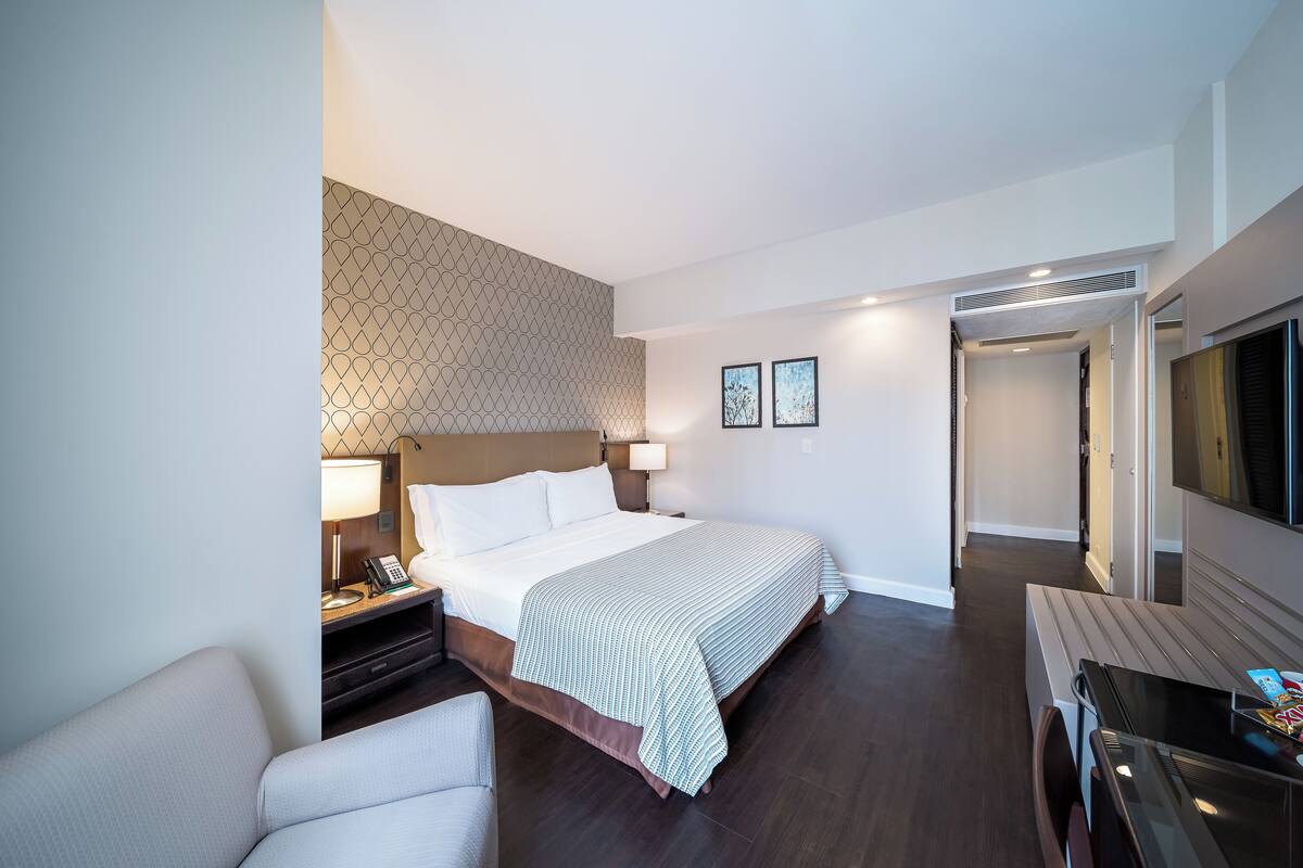 Una habitación de hotel con cama, mesita de noche, lámpara y televisor.