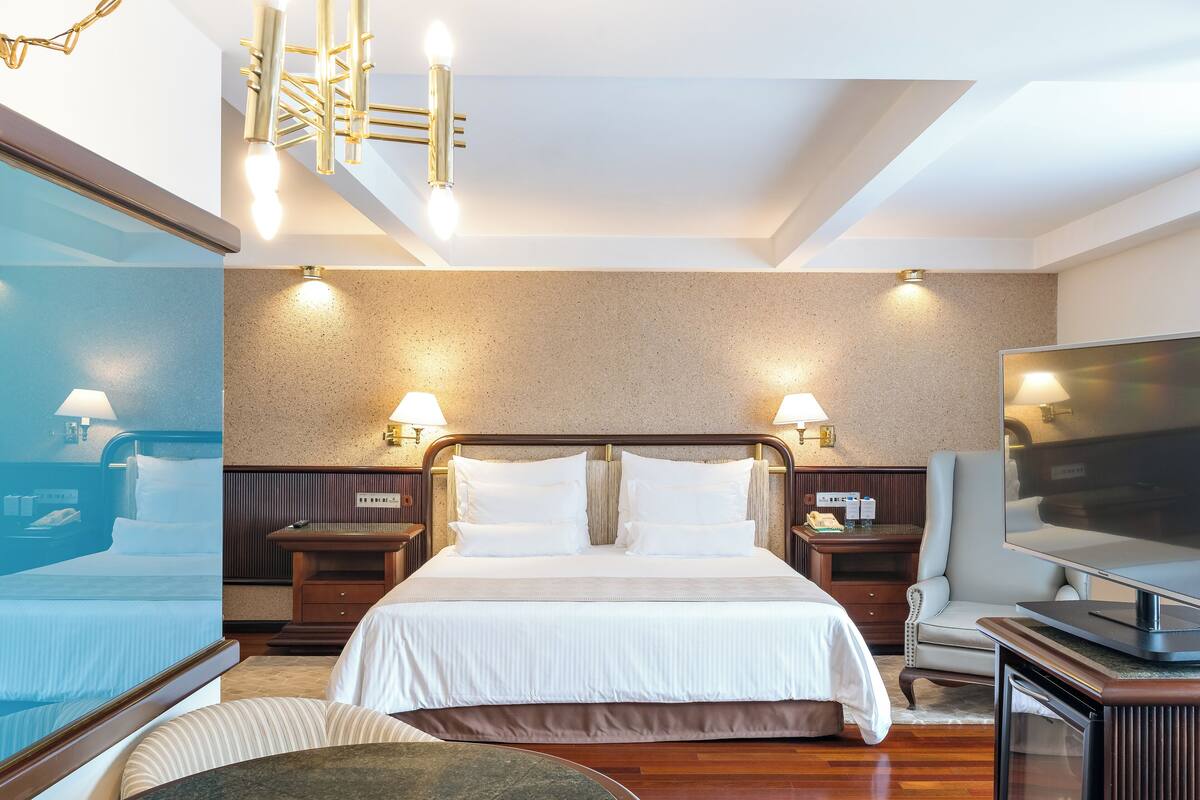 Una habitación de hotel con una cama grande, mesitas de noche, televisión y un área de descanso con una mesa y sillas.