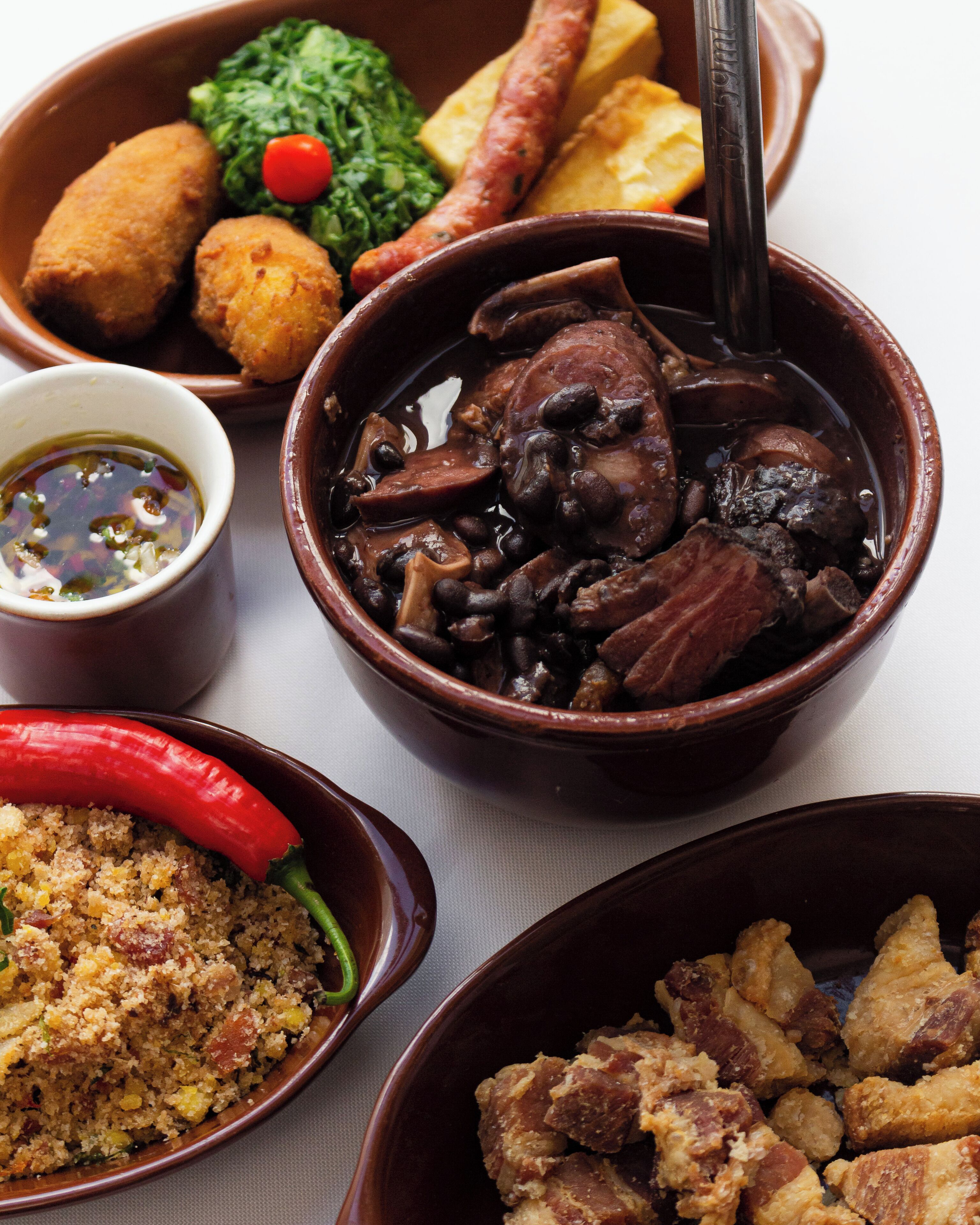 A variety of dishes including a bowl of stew with beans and meat, a bowl of couscous, and a bowl of fried items.