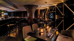 Un área de bar moderna con un diseño elegante, que incluye una barra, asientos e iluminación ambiental.