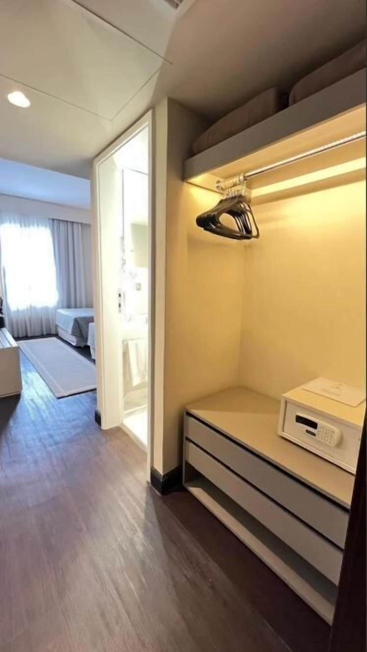 A modern hotel room with a walk-in closet, a bed, a desk, and a window with curtains.