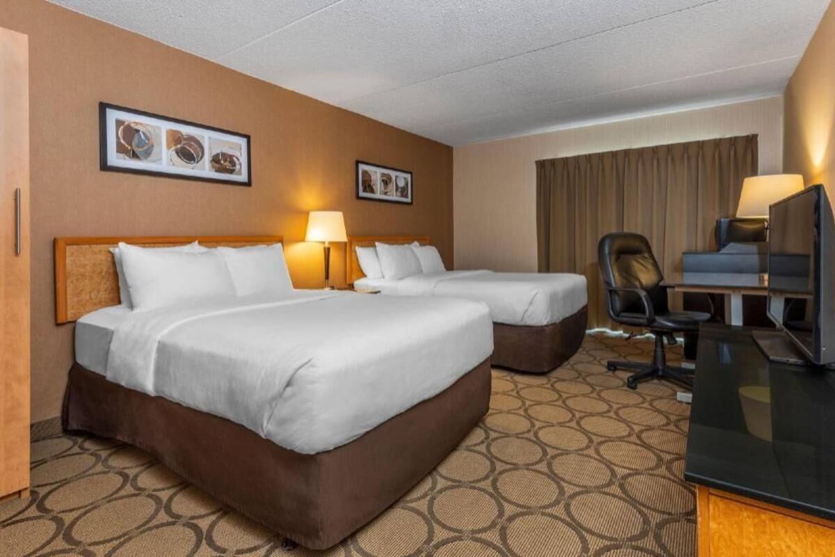 A hotel room with two beds, a desk, a chair, and a television.