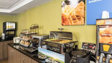 Montaje de bufé con diversos alimentos, una máquina de café y un cartel anunciando el desayuno.
