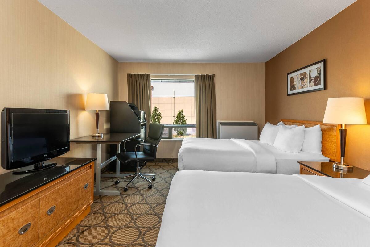 A hotel room with two beds, a desk with a TV, a chair, and a window with curtains.