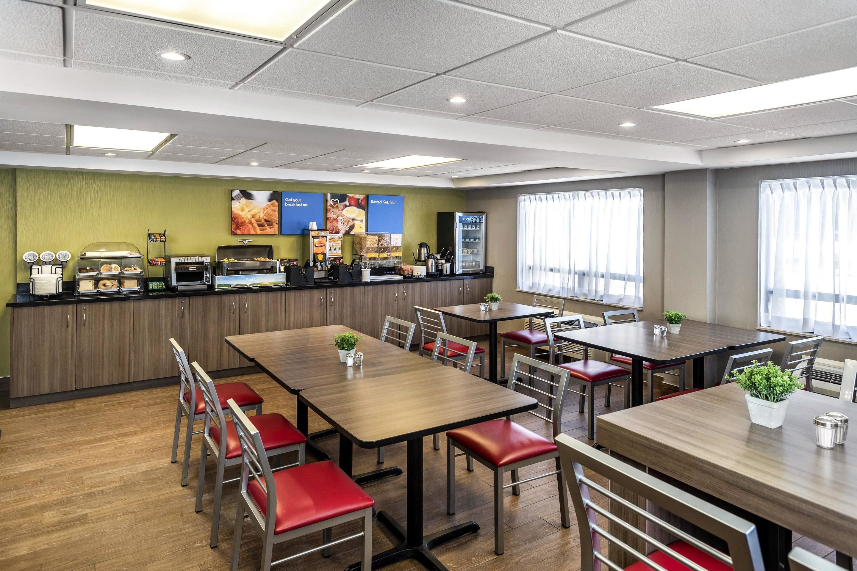 A restaurant with wooden tables and red cushioned chairs, a counter with food items, and a green wall with menu posters.