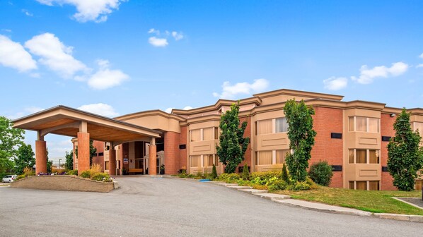Classic hotel with a central entrance under a covered walkway, surrounded by lush greenery.