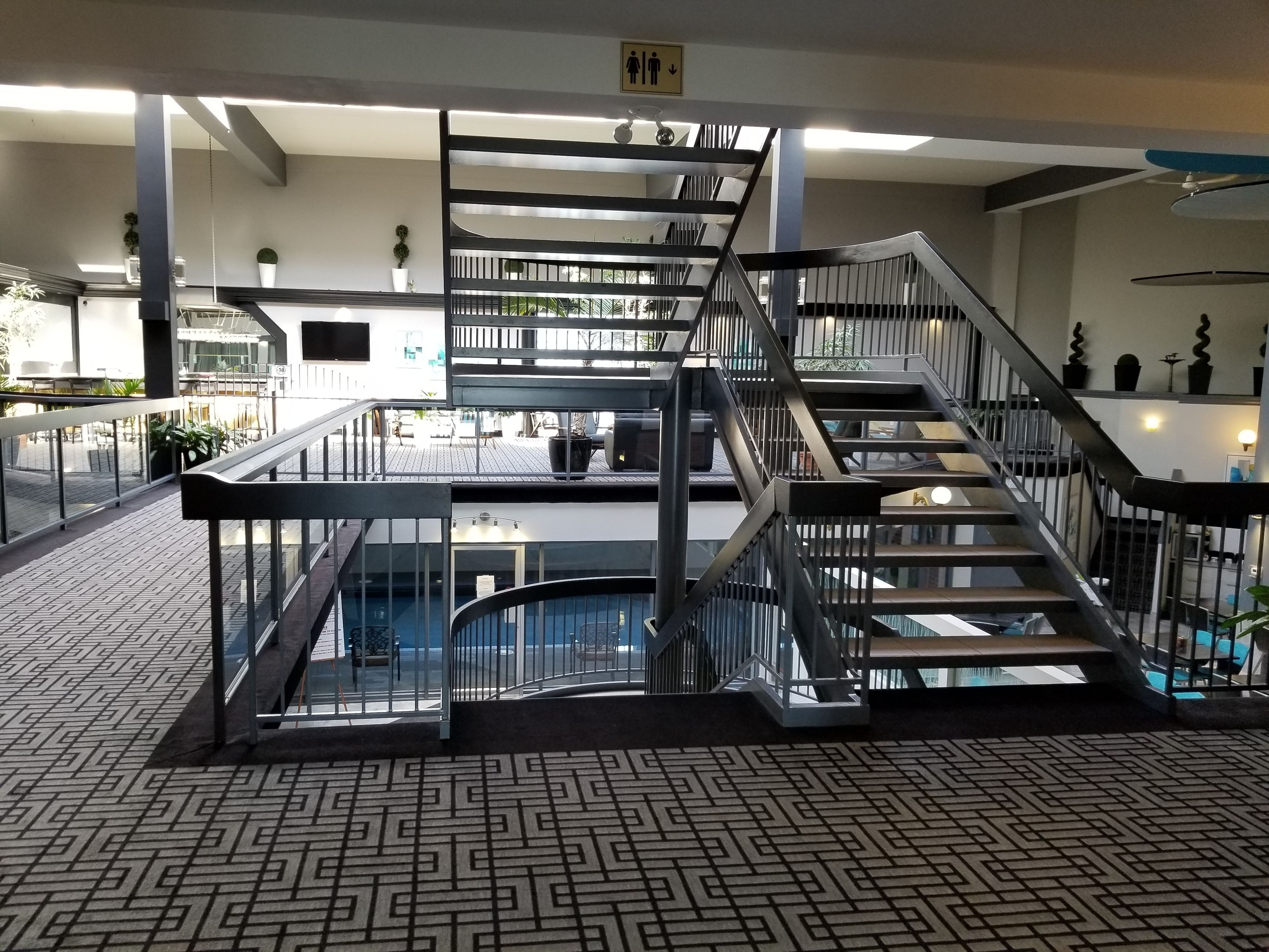 A modern indoor area with a central staircase, glass railings, and a patterned floor.