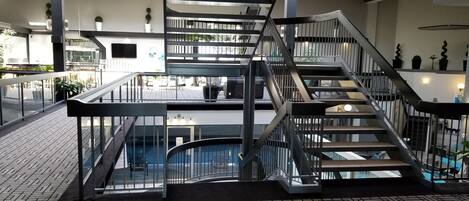 Um espaço interior moderno com uma escadaria central, guarda-corpos de vidro e piso estampado.