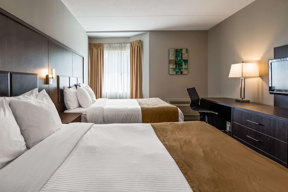 A hotel room with two beds, a desk, a chair, a television, and a painting on the wall.